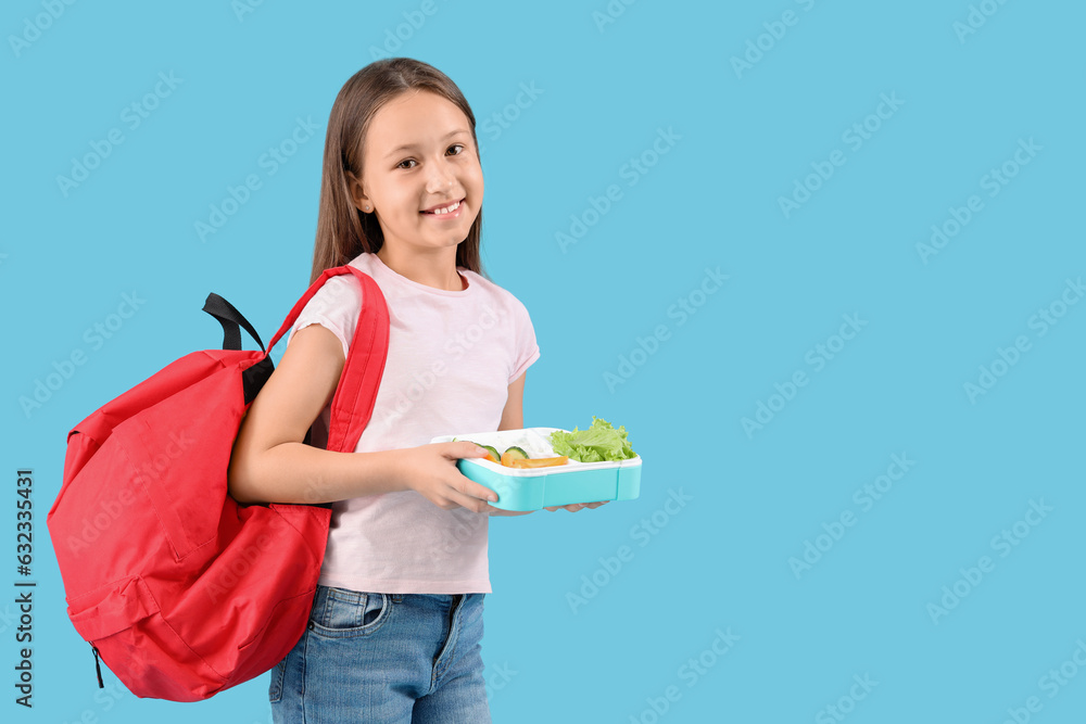 Happy little girl with backpack and lunchbox on blue background