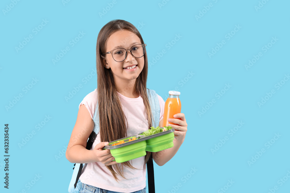 Happy little girl with bottle of juice and lunchbox on blue background