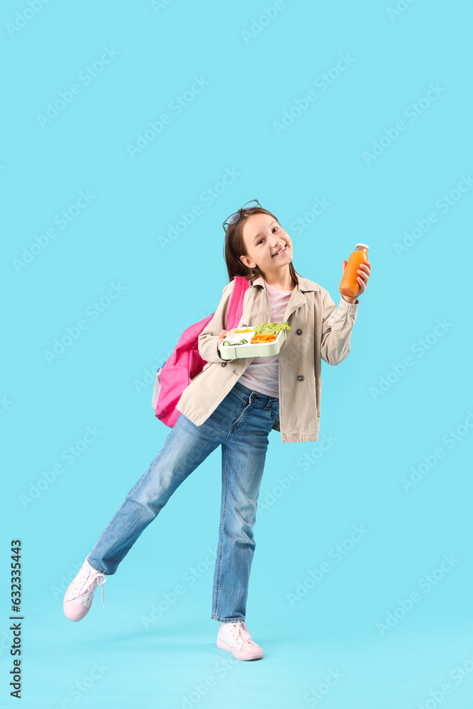 Happy little girl with bottle of juice and lunchbox on blue background