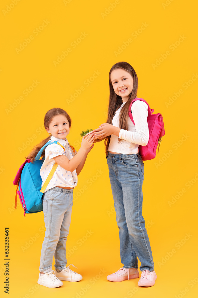 Happy girls with backpacks and lunchbox on yellow background