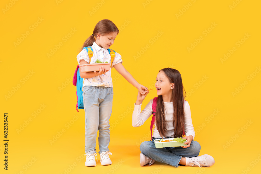 Happy girls with backpacks and lunchboxes on yellow background