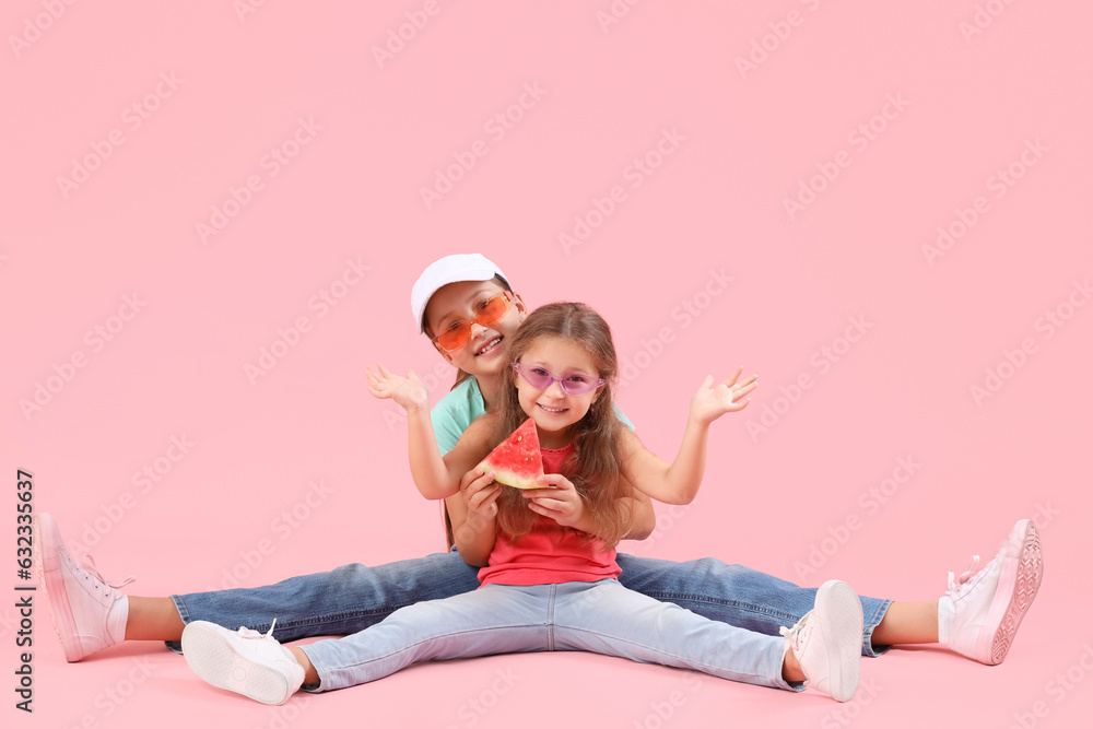 Happy little girls with slice of fresh watermelon sitting on pink background