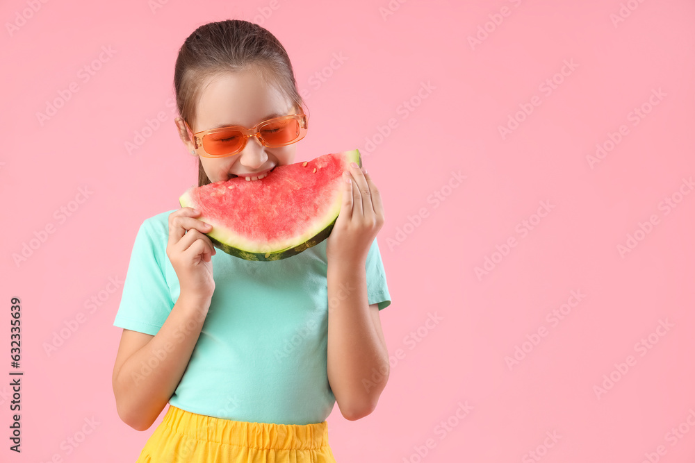 Happy little girl in sunglasses eating fresh watermelon on pink background