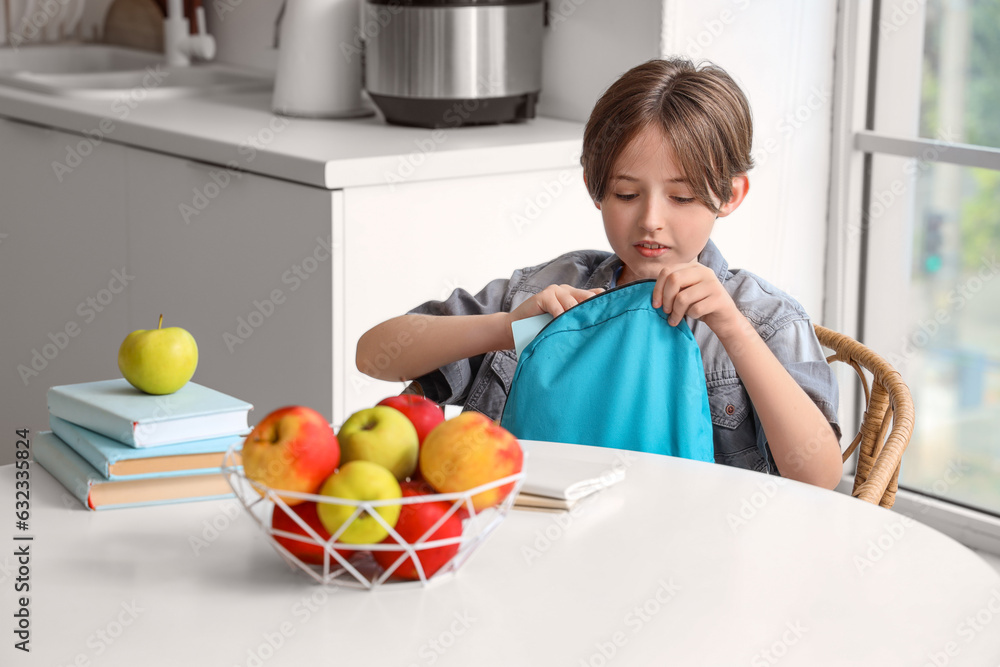 Little boy putting notebooks in schoolbag at home