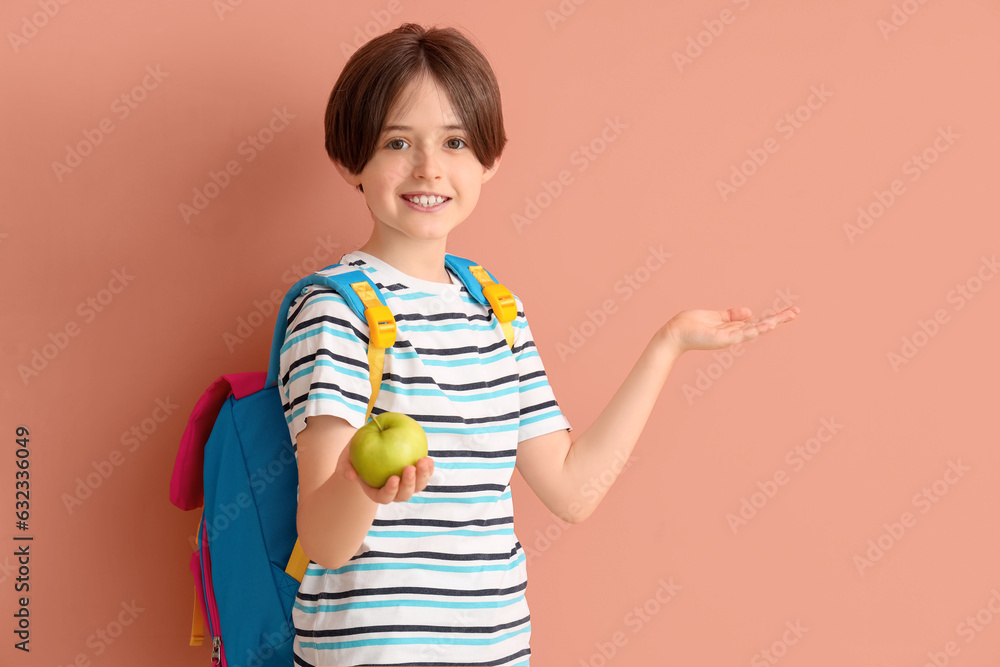 Happy little boy with backpack and fresh apple on color background