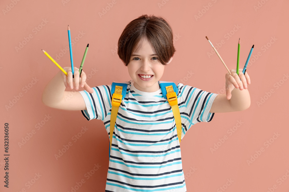 Happy little boy with backpack and stationery on color background