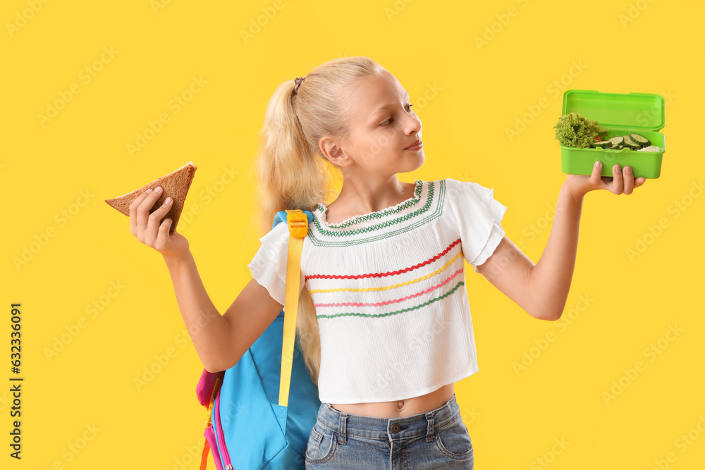 Happy girl with backpack, lunchbox and sandwich on yellow background