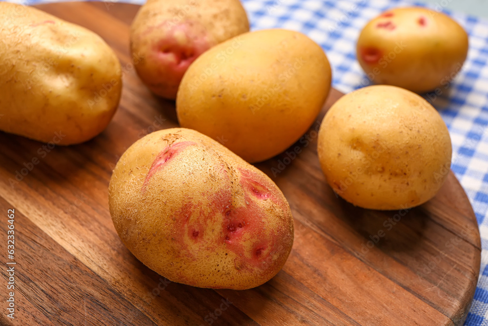 Wooden board with fresh raw potatoes on table, closeup