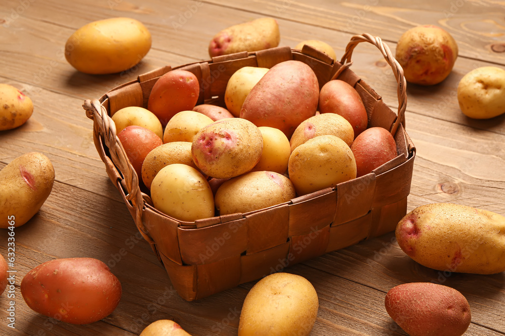 Wicker basket with fresh raw potatoes on wooden background