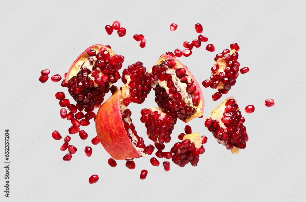 Flying fresh pomegranates with seeds on grey background