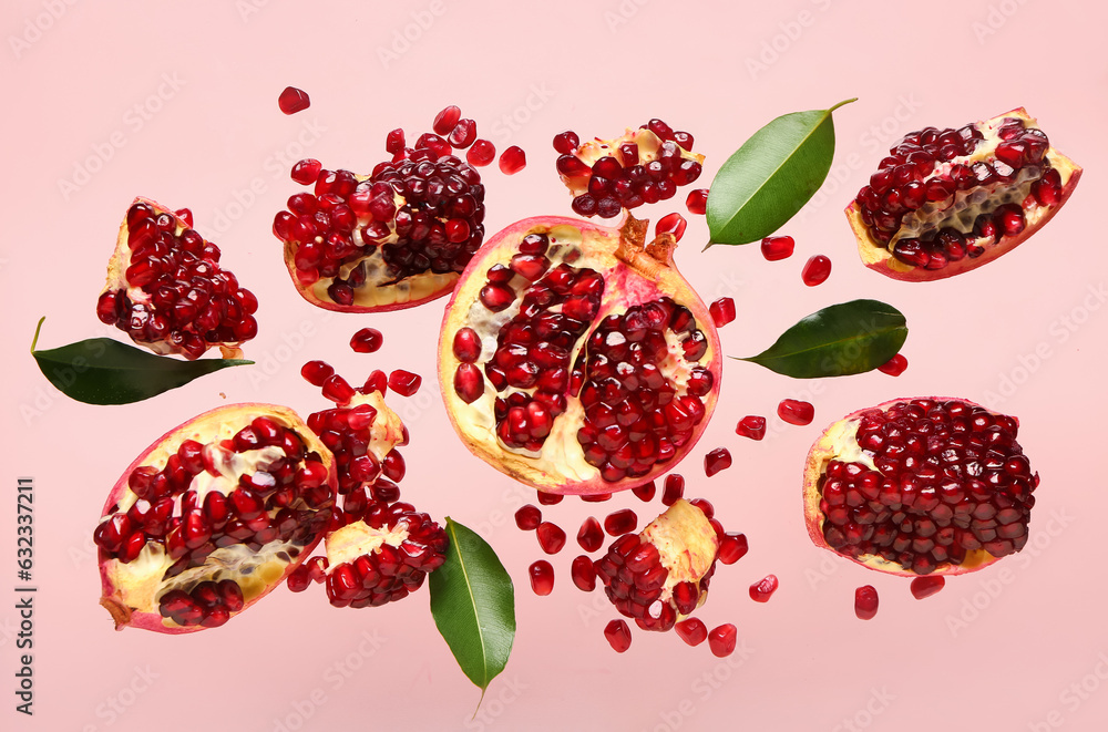 Flying fresh pomegranates with seeds and leaves on pink background