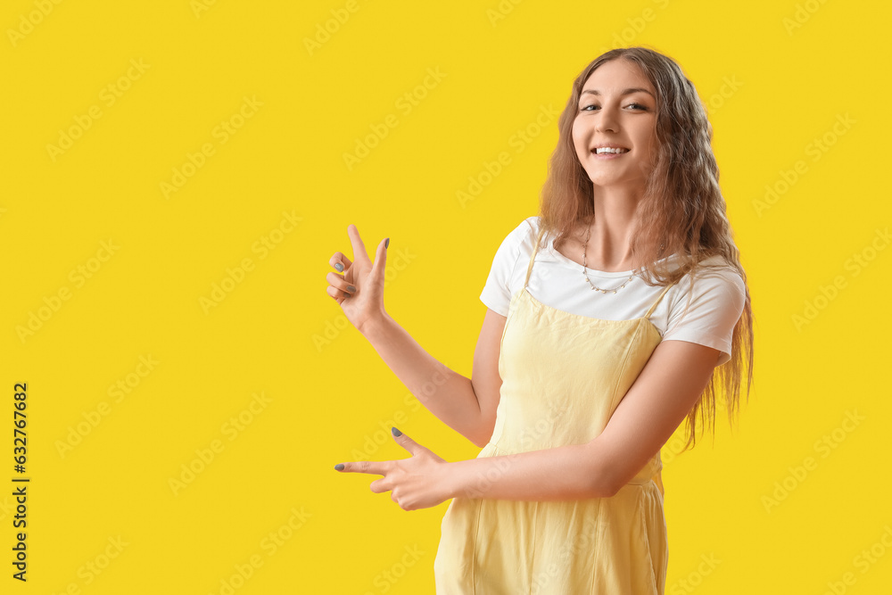 Beautiful young woman pointing at something on yellow background