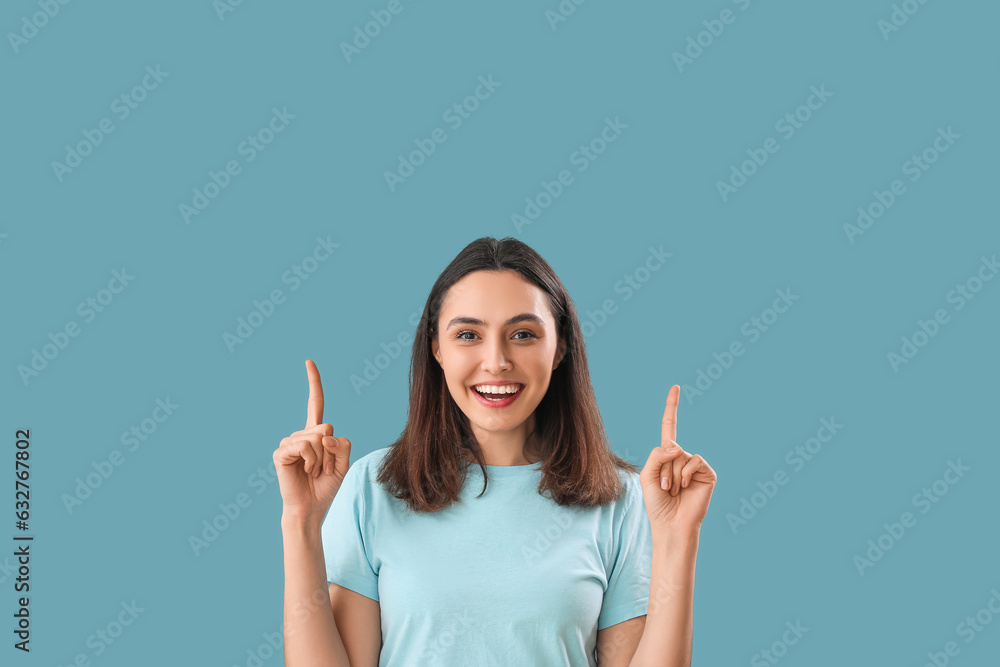 Young woman pointing at something on blue background