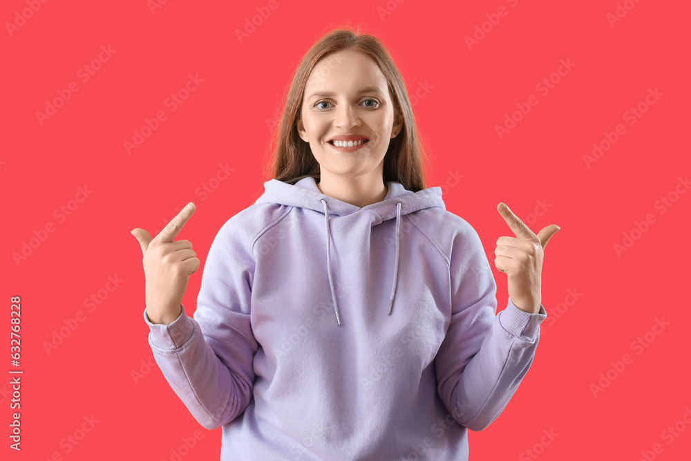 Beautiful redhead woman in hoodie pointing at herself on red background