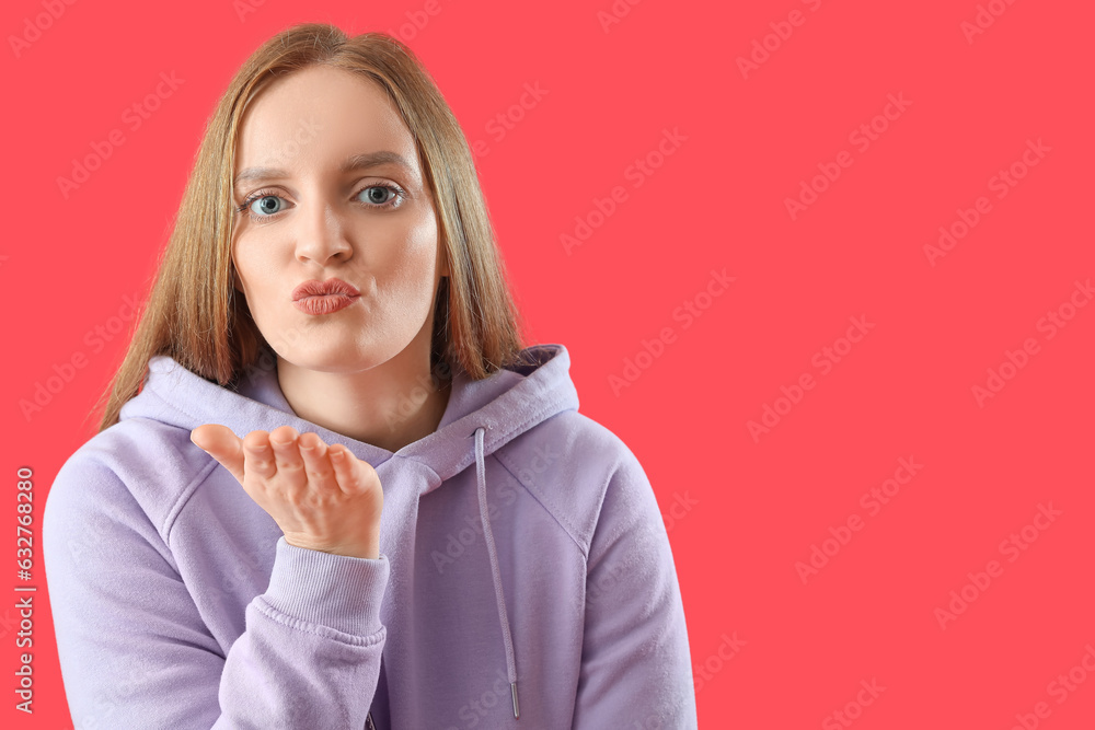 Beautiful redhead woman in hoodie blowing kiss on red background, closeup