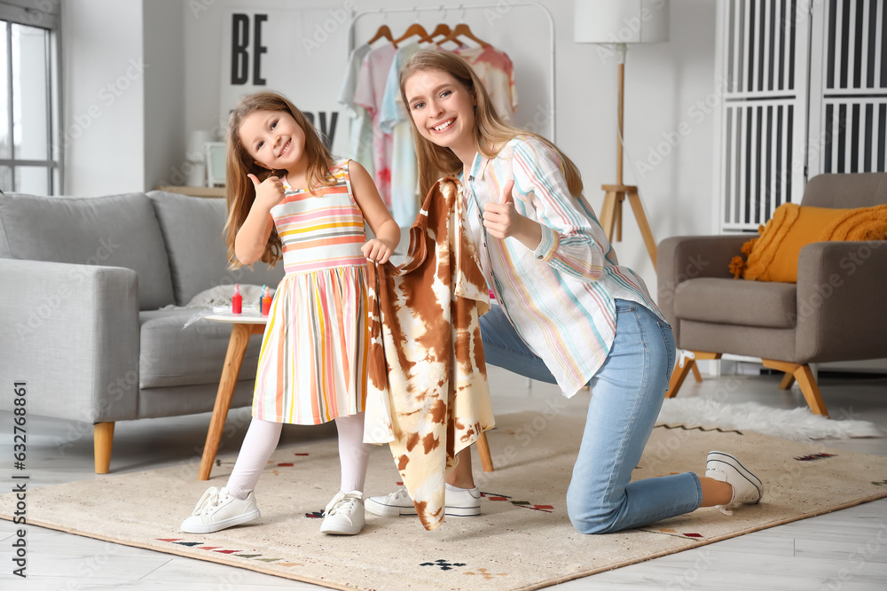 Little girl with her sister and tie-dye t-shirt showing thumbs-up at home