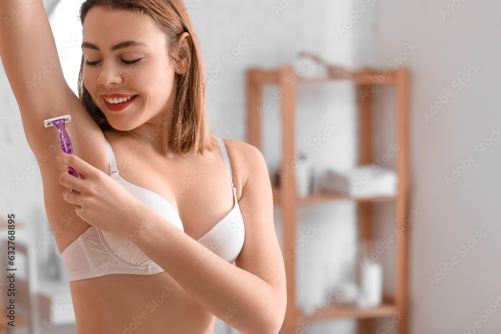 Young woman shaving her armpit with razor in bathroom