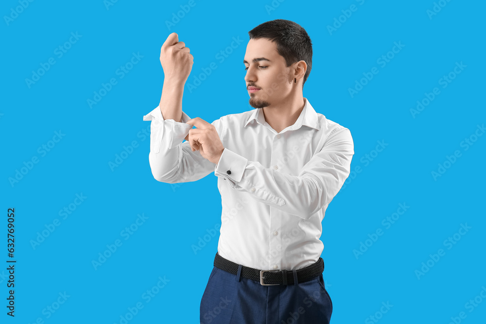 Young businessman rolling up his sleeve on light blue background