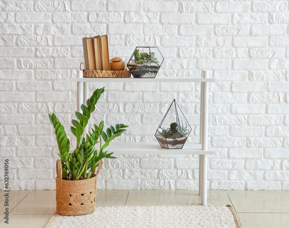 Shelving unit with florariums and books near white brick wall in room