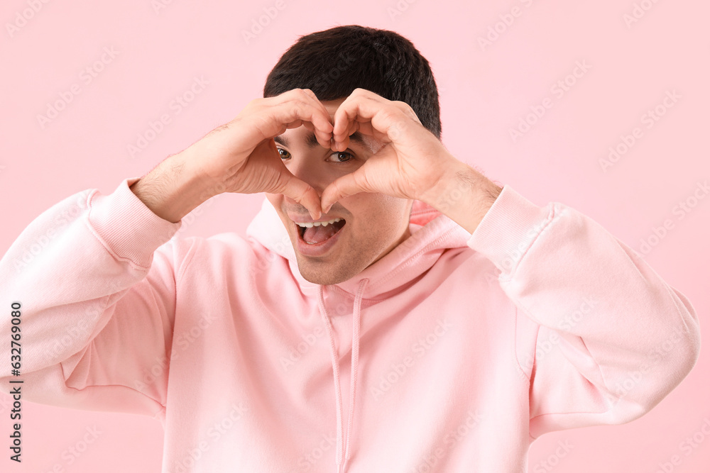 Young man making heart with his hands on pink background, closeup