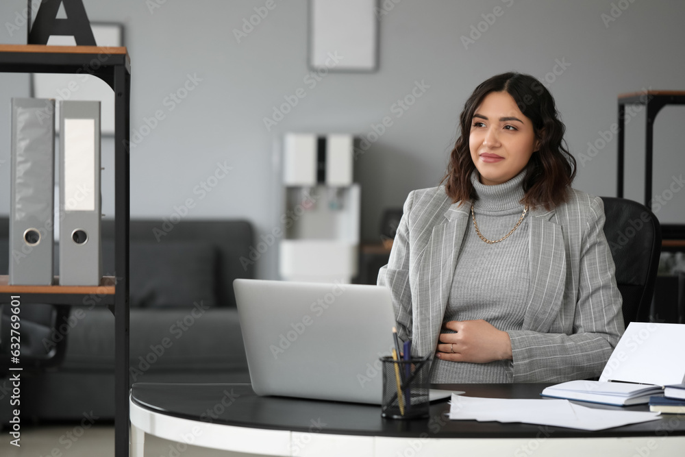 Young pregnant woman working at table in office