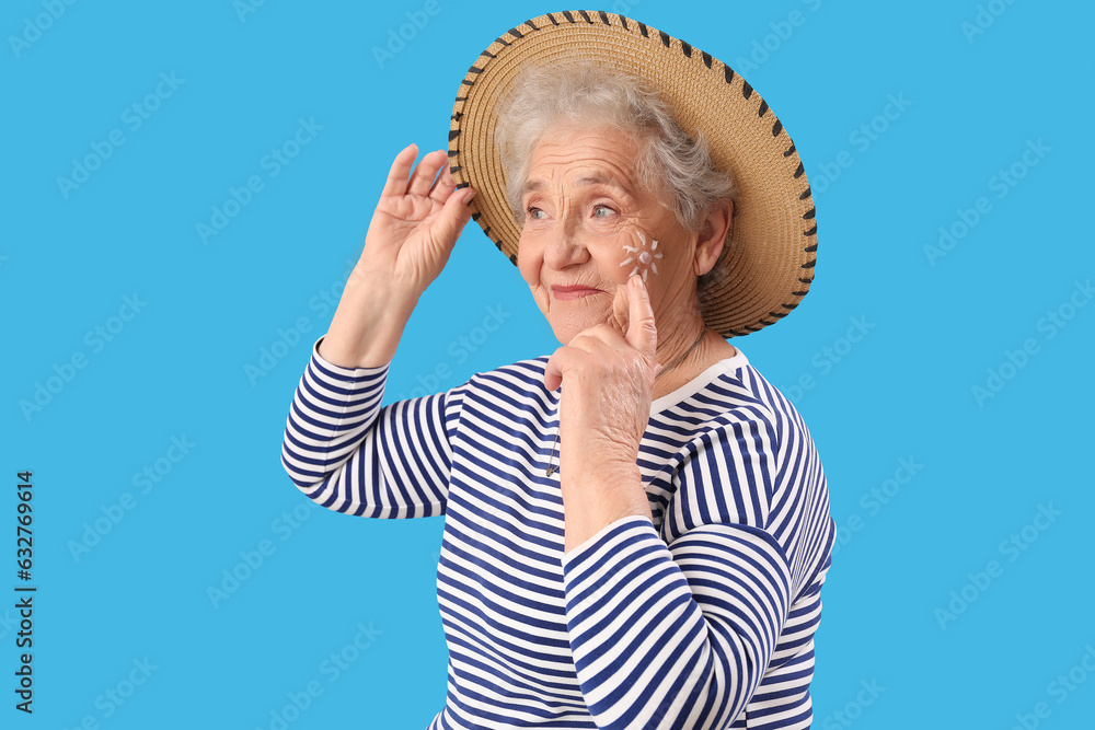 Senior woman with sun made of sunscreen cream on her face against blue background