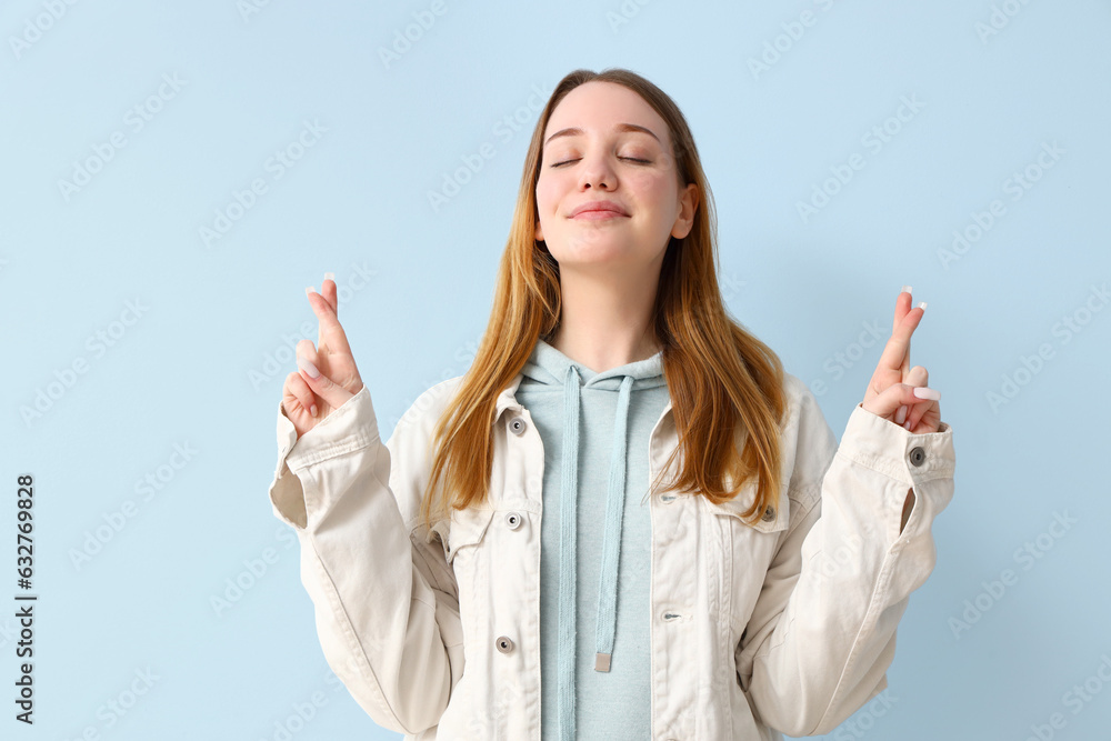 Beautiful young woman crossing fingers on blue background