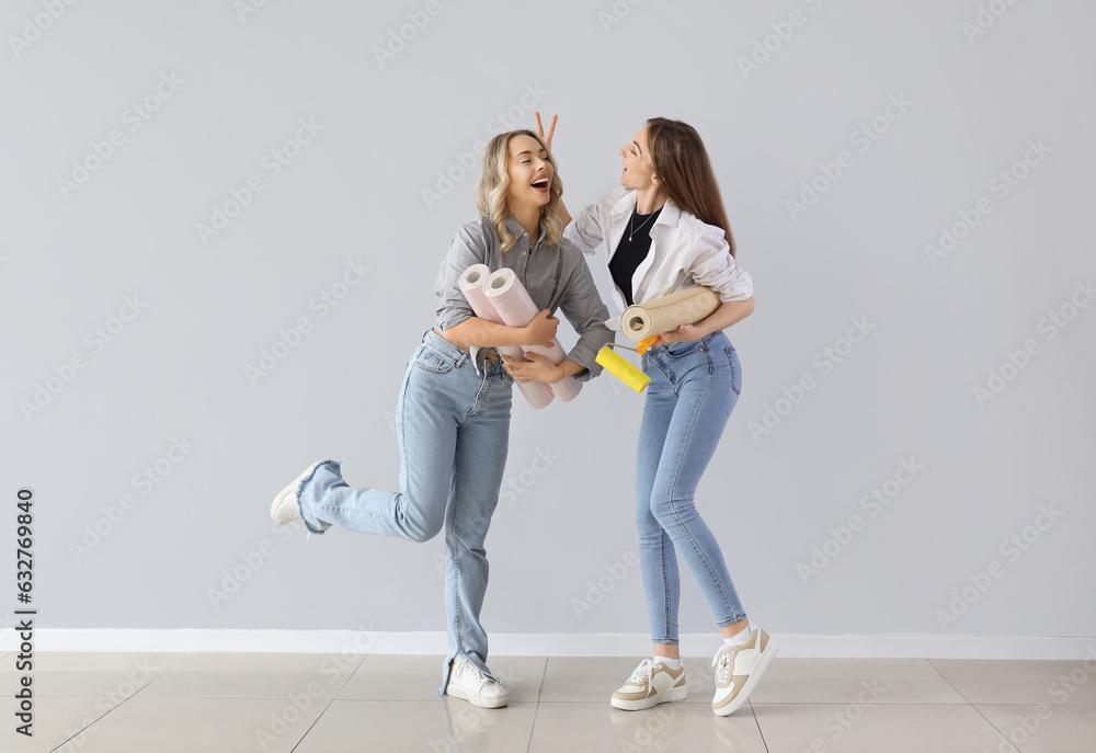 Young women with wallpaper rolls near grey wall