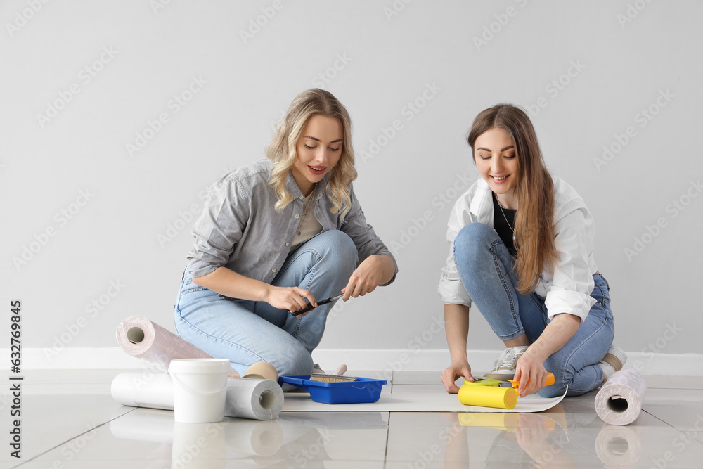 Young women with wallpaper rolls near grey wall