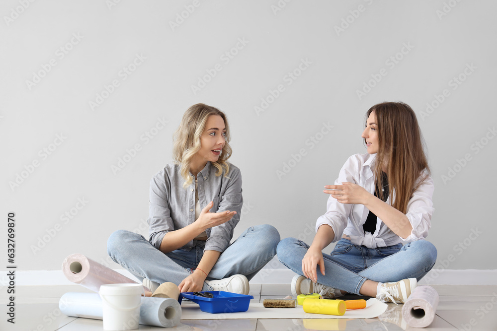 Young women with wallpaper rolls sitting near grey wall