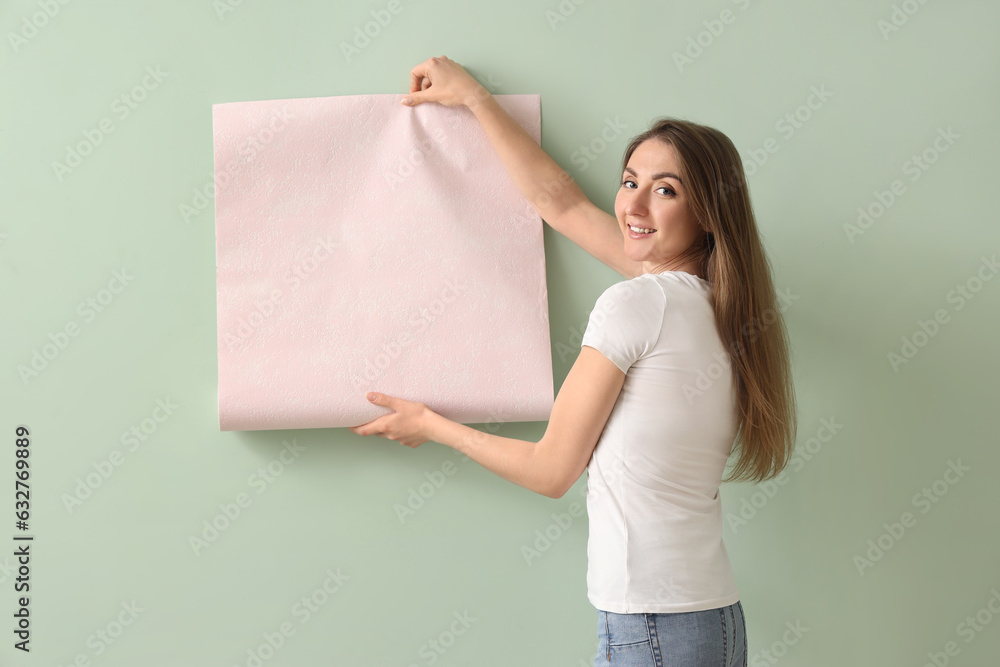 Young woman with wallpaper roll on green background