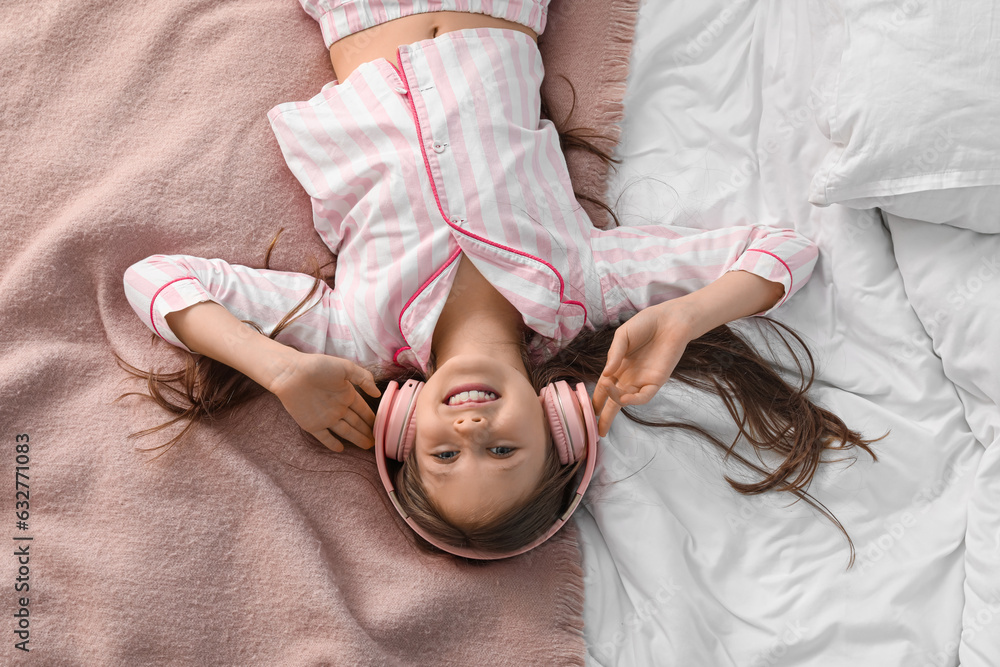 Little girl with headphones lying on bed, top view