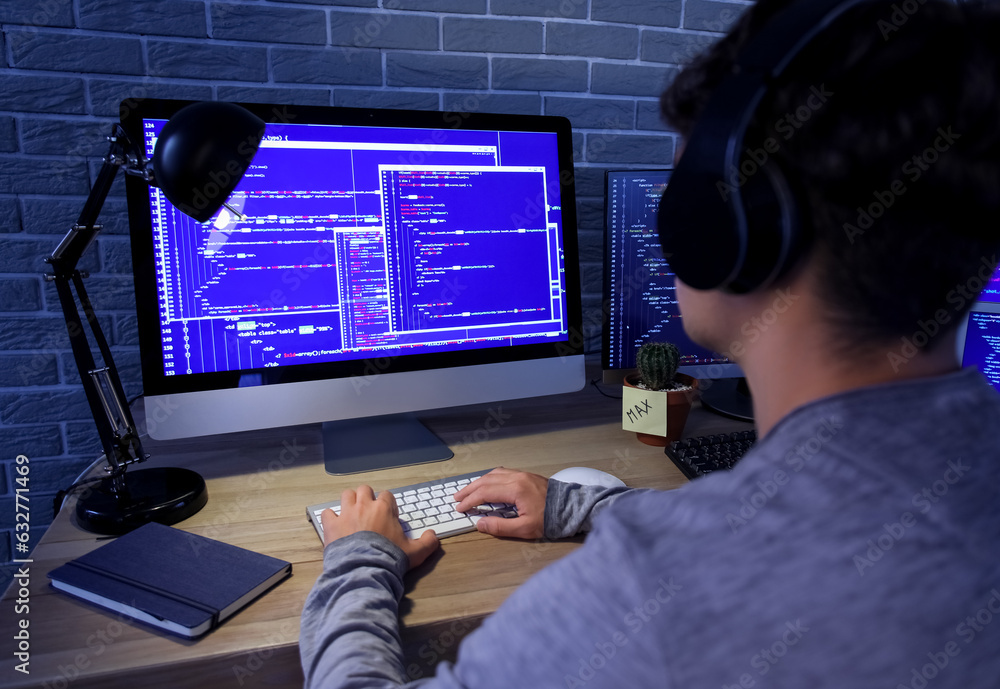 Male programmer working with headphones and computer in office at night