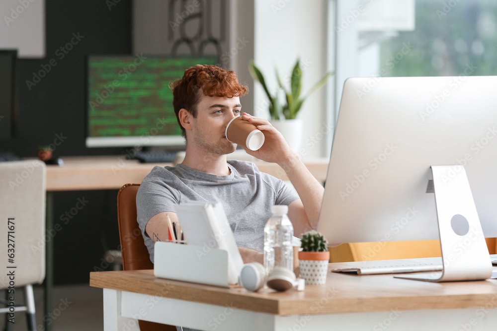 Male programmer drinking coffee at table in office