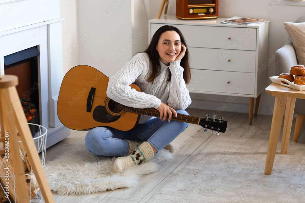 Young woman playing guitar near fireplace at home