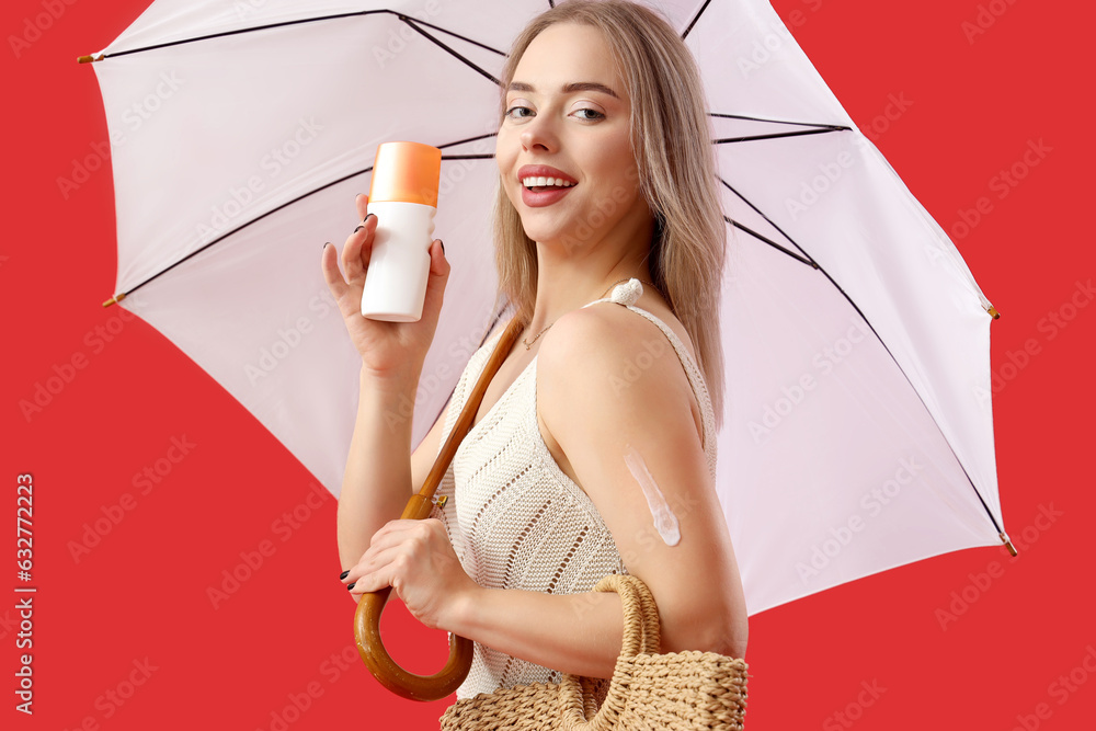 Young woman with sunscreen cream, umbrella and bag on red background