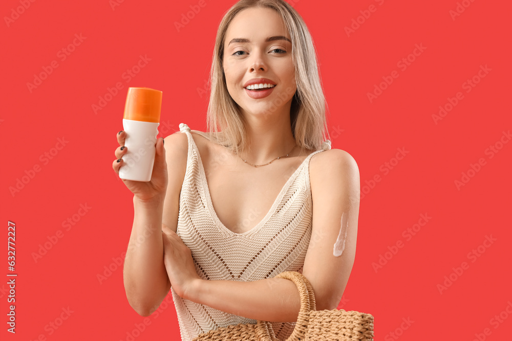 Young woman with sunscreen cream and bag on red background