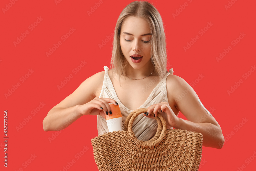 Young woman taking sunscreen cream out of bag on red background