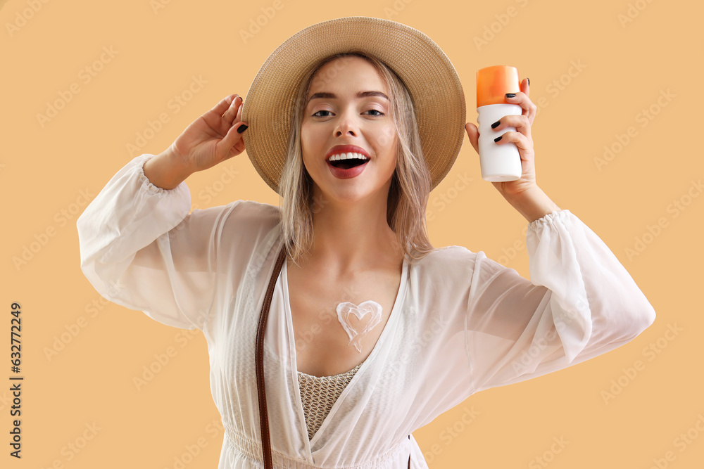 Young woman with heart made of sunscreen cream on beige background