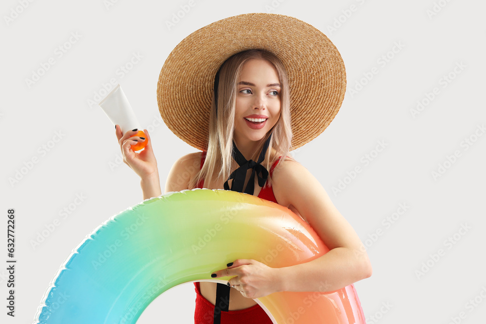 Young woman with sunscreen cream and inflatable ring on light background