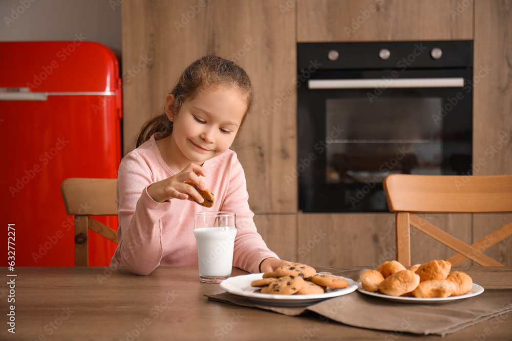 Little girl with cookie and glass of milk in kitchen