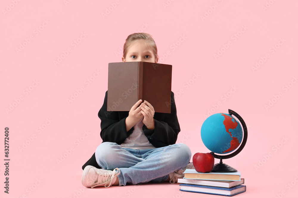 Little schoolgirl with books, globe and apple on pink background