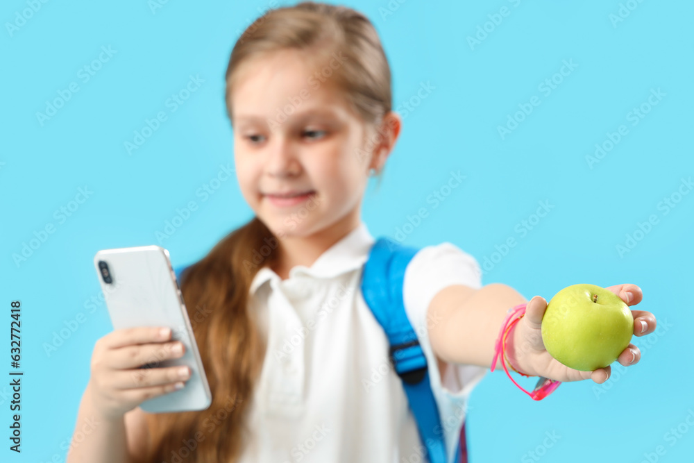 Little schoolgirl with smartphone and apple on light blue background