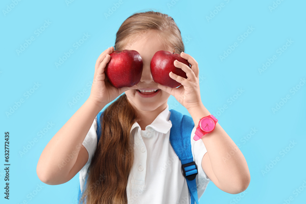 Funny little schoolgirl with apples on light blue background