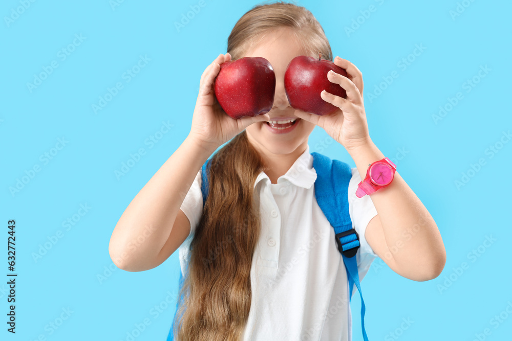 Funny little schoolgirl with apples on light blue background