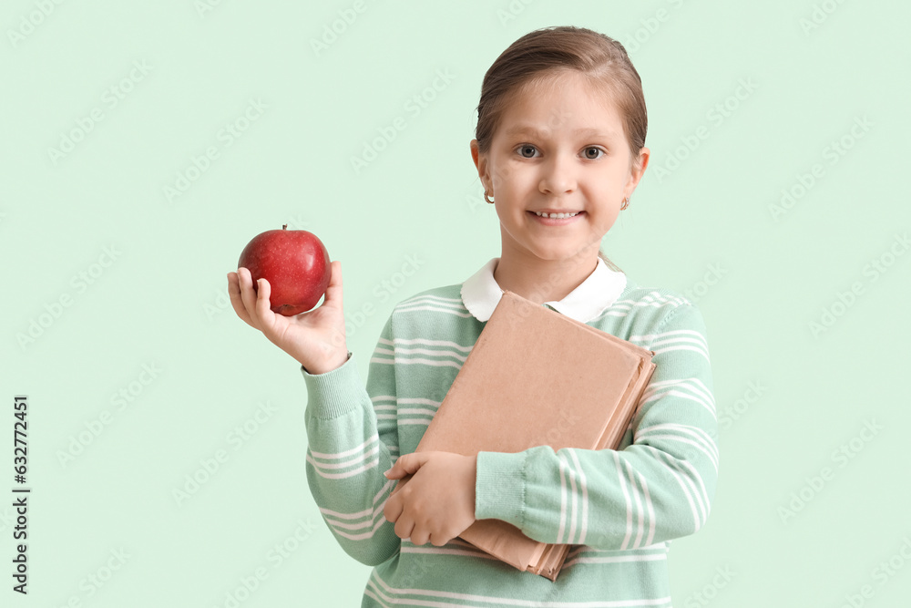 Little schoolgirl with books and apple on mint background