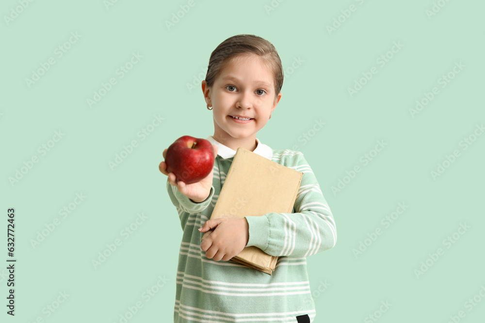 Little schoolgirl with books and apple on mint background