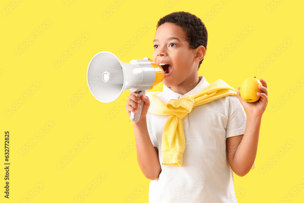 Little African-American boy with megaphone and apple on yellow background