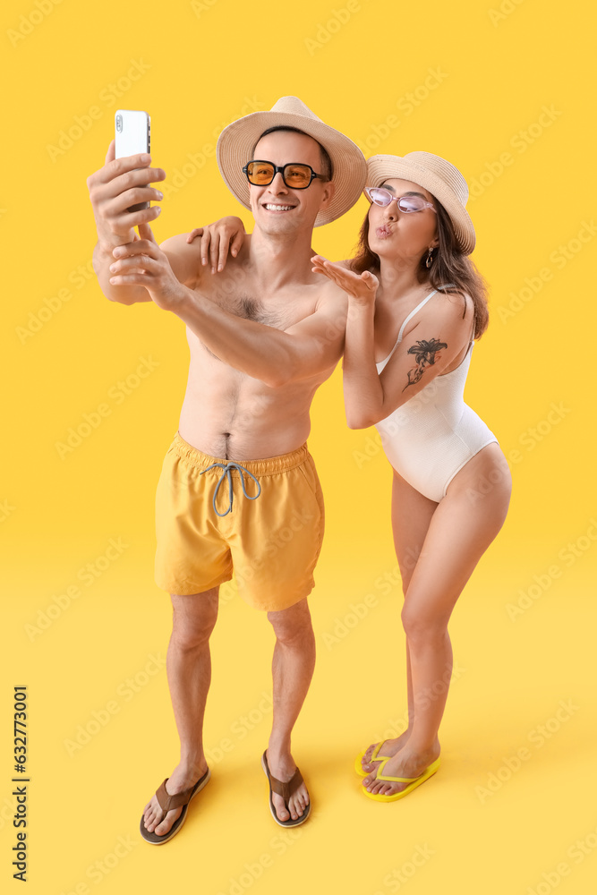 Young couple in summer hats taking selfie on yellow background