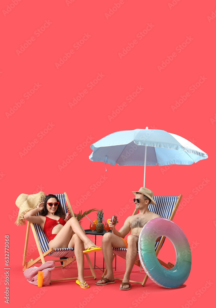 Young couple with strawberries in deck chairs and beach accessories on red background